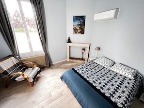 Ein Schlafzimmer mit Bett, Sessel, Schreibtisch mit Statue, Fenster und einem Gemälde an der Wand.