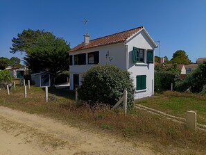 Ein weißes, zweistöckiges Haus mit rotem Ziegeldach, grünen Fensterläden und einer kleinen angebauten Garage.