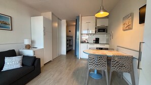 A compact living space with a kitchenette, a dining area with a table and chairs, a sofa with cushions, and a hanging light fixture. - Charming studio - 4 guests, 2 mins to beach (Urrugne)