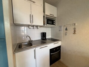 A compact kitchen with white cabinets, a stainless steel sink, a microwave, and a coffee maker.
