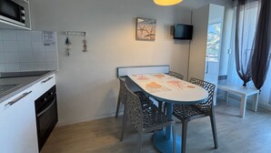 A compact kitchen with a dining area, a TV mounted on the wall, and a window with curtains. - Charming studio - 4 guests, 2 mins to beach (Urrugne)