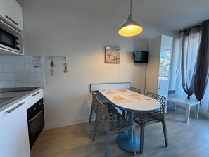 Uma cozinha compacta com área de refeições, uma TV fixada na parede e uma janela com cortinas.