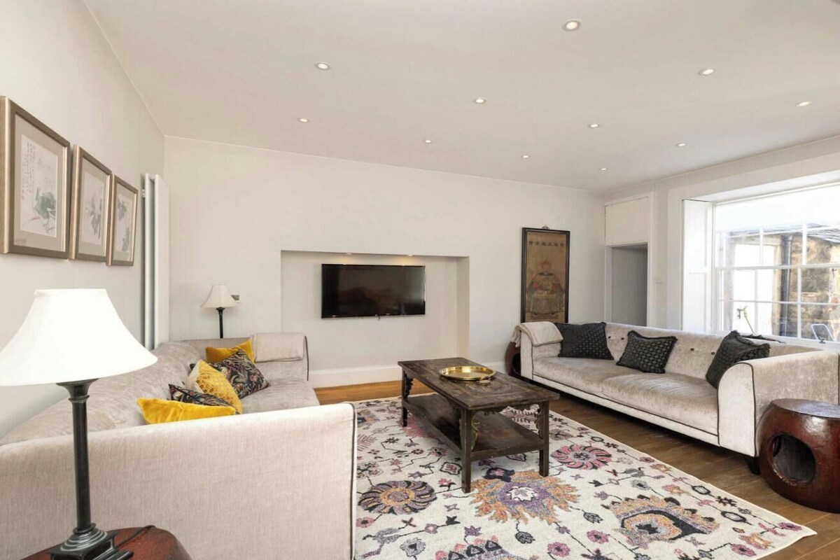 Ein Wohnzimmer mit einer Couch, einem Couchtisch, einer Lampe und einem an der Wand befestigten Fernseher.