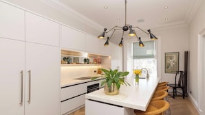 A modern kitchen with white cabinetry, a central island with bar stools, and a pendant light fixture. - Saxecoburg Residence Place (Edinburgh)