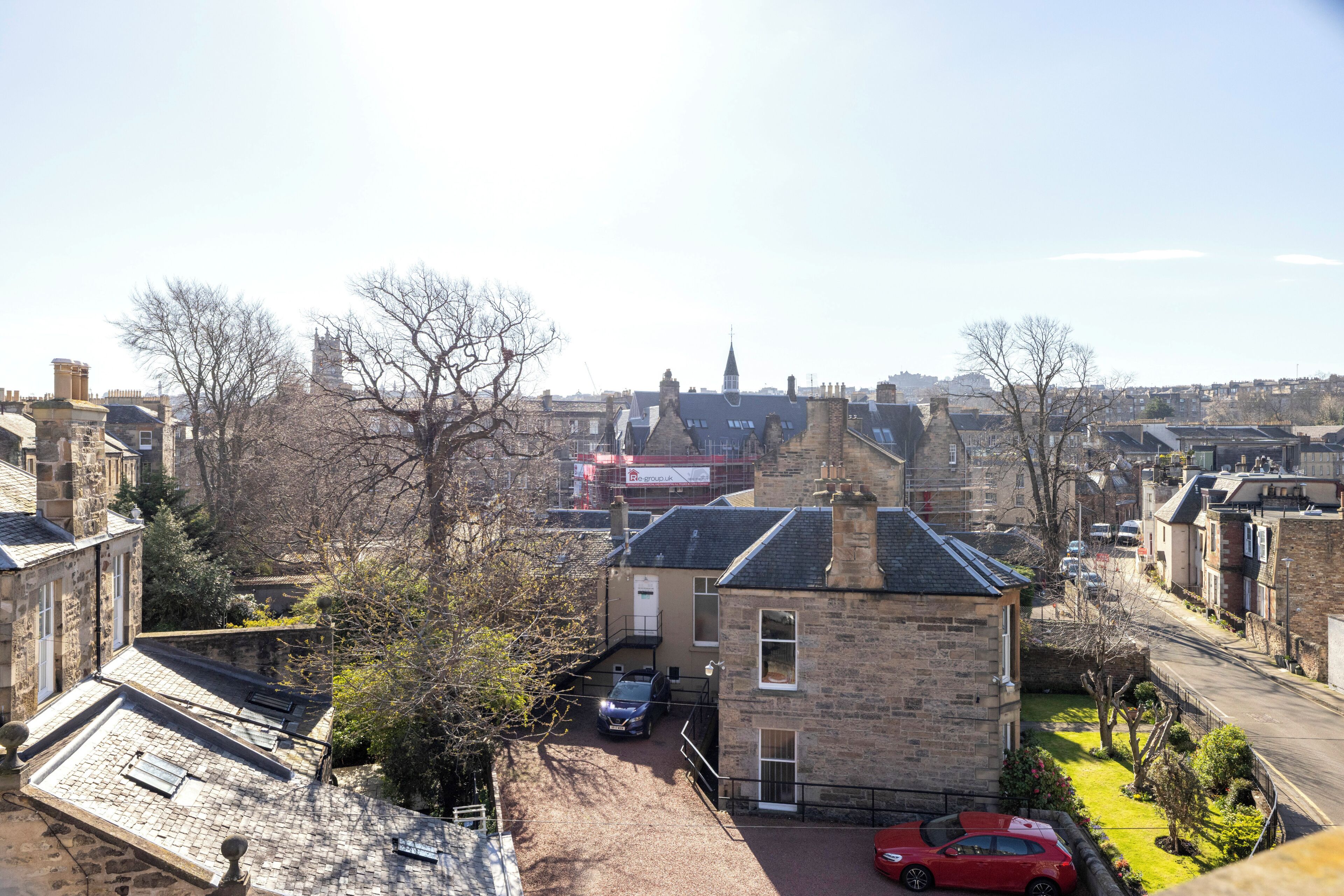A residential area with stone buildings, a red car parked on the street, and a clear sky.