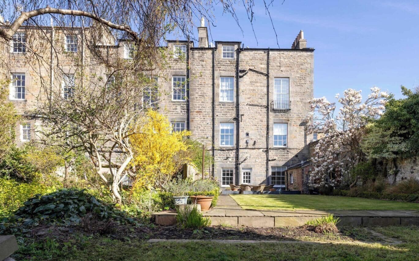 A stone building with multiple windows and a lawn in the foreground.