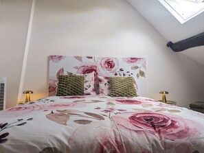 Ein Schlafzimmer mit schrägem Dach, einer blumigen Bettdecke, zwei strukturierten Kissen und einem an der Wand hängenden Kunstwerk.