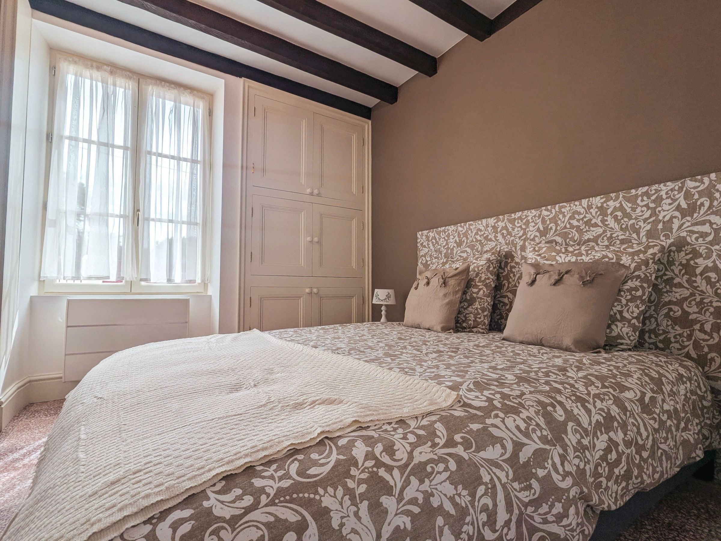 Une chambre avec un grand lit, une fenêtre avec des rideaux, une armoire et une tête de lit à motifs.