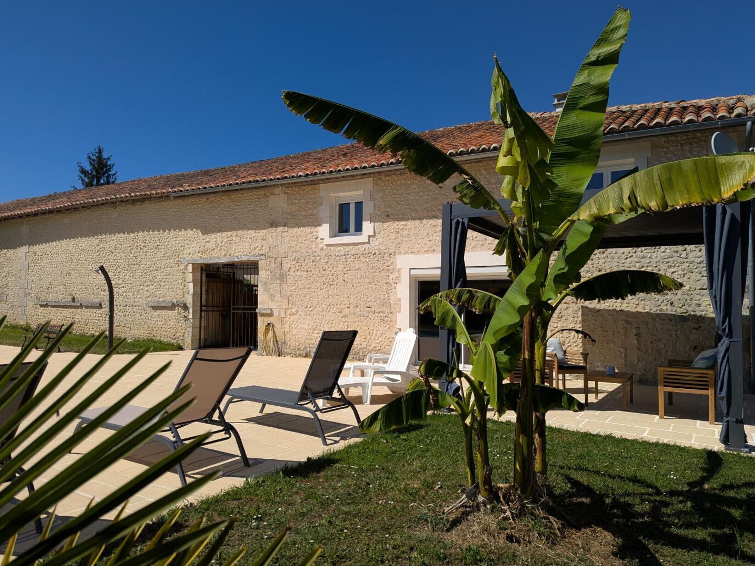 A stone building with a tiled roof, outdoor seating, and a banana plant.