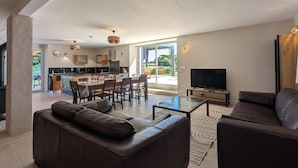 A modern living room with a sofa, a coffee table, and a TV. There's a dining area with chairs and a table, and a kitchen in the background. - House with private pool, pets - 8 guests (RONSENAC)