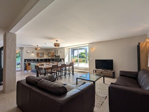 A modern living room with a sofa, a coffee table, and a TV. There's a dining area with chairs and a table, and a kitchen in the background. - House with private pool, pets - 8 guests (RONSENAC)