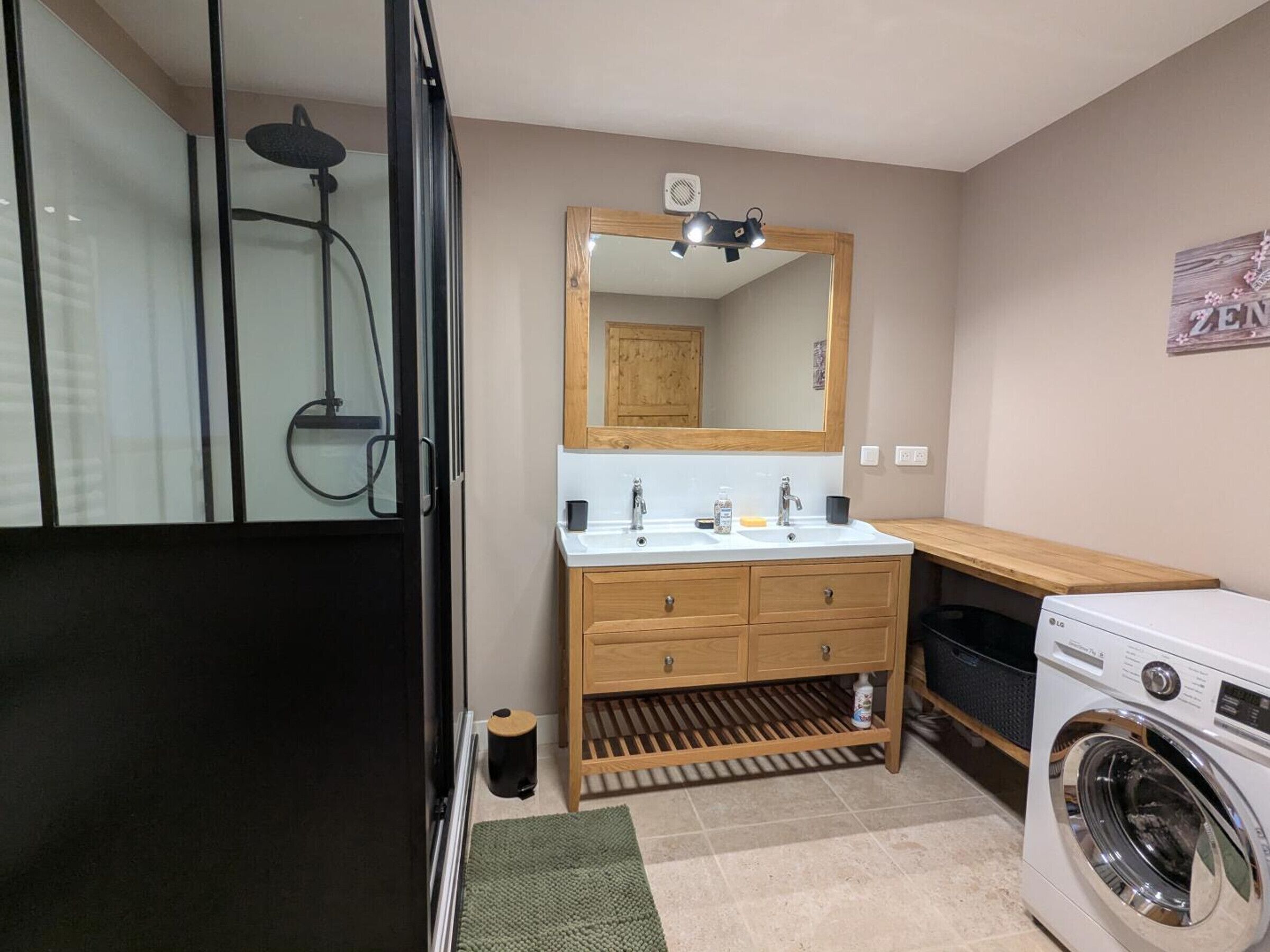 Un bany compacte amb dutxa, un lavabo amb mirall, una rentadora i un petit cubell de basures.
