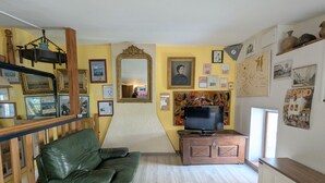Uma sala de estar com um sofá de couro verde, um aparador de madeira, uma televisão e diversas molduras com quadros nas paredes.