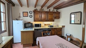 Uma cozinha compacta com fogão a gás, micro-ondas e máquina de lavar louça, armários de madeira e um espaço de refeições com toalha de mesa estampada.