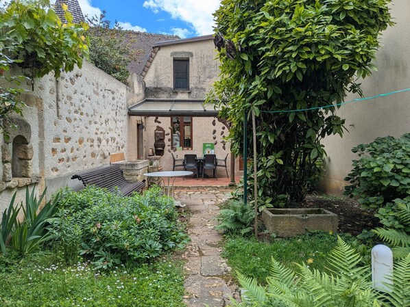 A stone building with a patio area, outdoor seating, and a garden with ferns and white flowers.