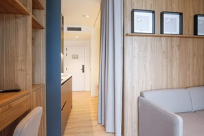 A modern hotel room with a wooden wardrobe, a desk, a sofa, and framed pictures on the wall.