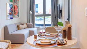 Una sala de estar moderna con comedor listo para una comida, que incluye un sofá, una mesa de comedor con platos y cubiertos, y obras de arte en las paredes.