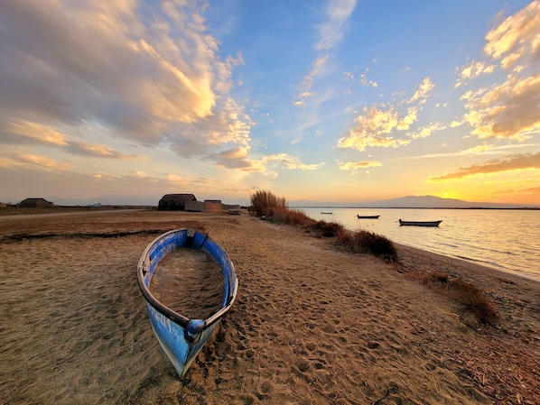 Ein Boot am sandigen Strand, im Hintergrund ein Sonnenuntergang.