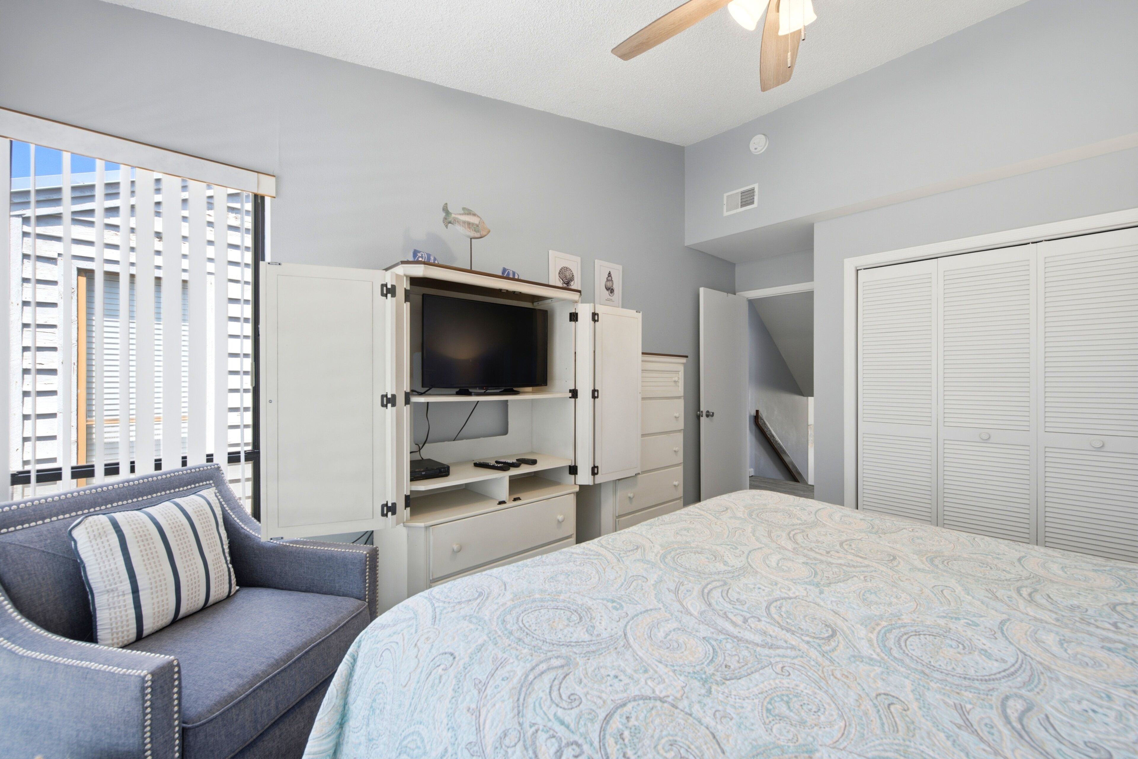 A bedroom with a bed, a sofa, a TV cabinet, a closet, and a window with blinds.