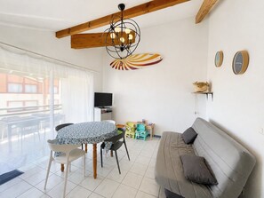 A living room with a sofa, a dining table with chairs, a TV, and a balcony with a view. - Apartment with ocean view - 6 guests (Vieux-Boucau-les-Bains)