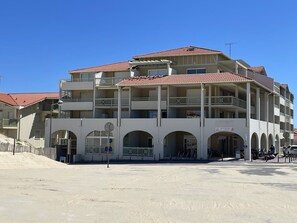Ein mehrstöckiges Hotel mit Balkonen, einem überdachten Eingang und sandigem Untergrund.