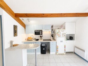 Eine kompakte Küche mit Mikrowelle, Spüle und Kühlschrank, ausgestattet mit hellblauen Schränken und einem Holzbalken an der Decke.