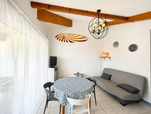 Ein Essbereich mit einem runden Tisch, Stühlen, einer Couch, einem Fernseher und einer Deckenleuchte.