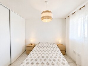 A bedroom with a bed, bedside lamps, a hanging light fixture, and a window with curtains. - Apartment with ocean view - 6 guests (Vieux-Boucau-les-Bains)