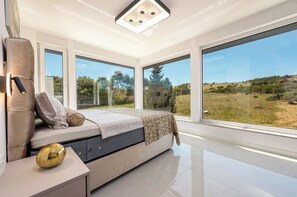 A modern bedroom with a large bed, a bedside table with a decorative object, and a view of a natural landscape through large windows. - Villa Weiss 1 (Vir)