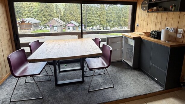 A compact kitchen with a dining area, large windows, and a view of a residential area. - Studio in the heart of the station - pets welcome (Le Lioran)