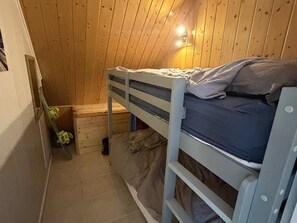 Ein kleines Zimmer mit einem einzelnen Bett, Holzwänden und einer geneigten Decke.