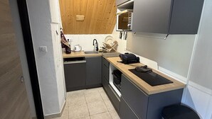 A compact kitchen with grey cabinets, a wooden countertop, a sink, and a dishwasher. - Studio in the heart of the station - pets welcome (Le Lioran)