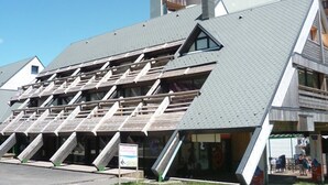 A building with a unique triangular roof design, featuring multiple skylights and a visible entrance area with outdoor seating. - Studio in the heart of the station - pets welcome (Le Lioran)
