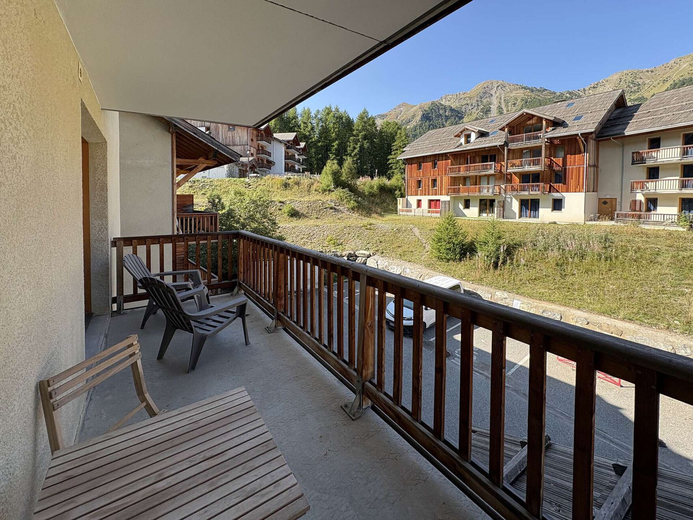 Een balkon met houten meubels, een uitzicht op een bergachtig landschap en gebouwen met balkons.