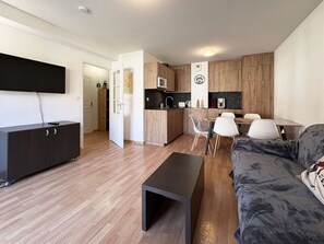 A modern living space with a flat-screen TV, a sofa, a coffee table, a kitchen area with wooden cabinets, and a dining table with chairs. - Apartment Les Orres 1800 with pool access, sleeps 6 (Les Orres)