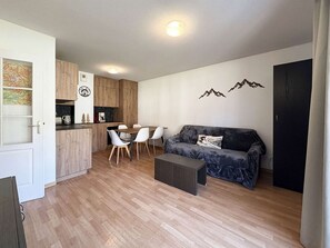 A modern living room with a sofa, a dining table with chairs, a kitchen area with wooden cabinets, and a small coffee table. - Apartment Les Orres 1800 with pool access, sleeps 6 (Les Orres)