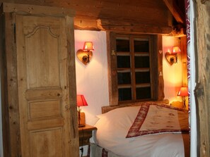 Ein Zimmer mit Holzboden, einem Bett, zwei Wandlampen und einem Fenster mit Spitzenvorhängen.