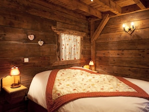 Un dormitorio de estilo cabaña de madera con cama, dos lámparas de noche, una ventana con cortinas florales y una decoración con forma de corazón en la pared.