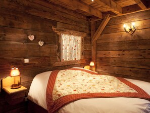 A wooden cabin-style bedroom with a bed, two bedside lamps, a window with floral curtains, and a heart-shaped decoration on the wall. - Spacious chalet with Wifi - 10 guests (Samoëns)