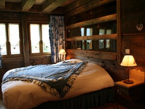 Une chambre dans une cabane en bois, avec un lit, deux lampes de chevet et une fenêtre avec des rideaux.