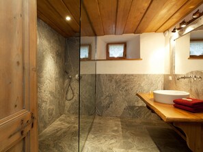 Ein Badezimmer mit Holzboden, Steinwänden, einer Dusche, einem Waschbecken und einem Spiegel.
