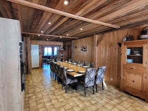 A dining area with a long wooden table, patterned chairs, and a wooden cabinet with glass doors. - Charming chalet with WiFi - 18 guests (Samoëns)