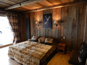 A wooden-paneled room with a bed, two wall-mounted lamps, and a deer painting. - Charming chalet with WiFi - 18 guests (Samoëns)