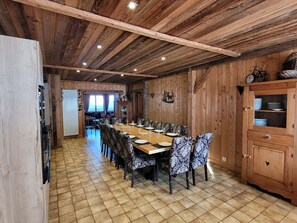 A dining area with a long wooden table, patterned chairs, and a wooden cabinet with glass doors. - Charming chalet with WiFi - 18 guests (Samoëns)