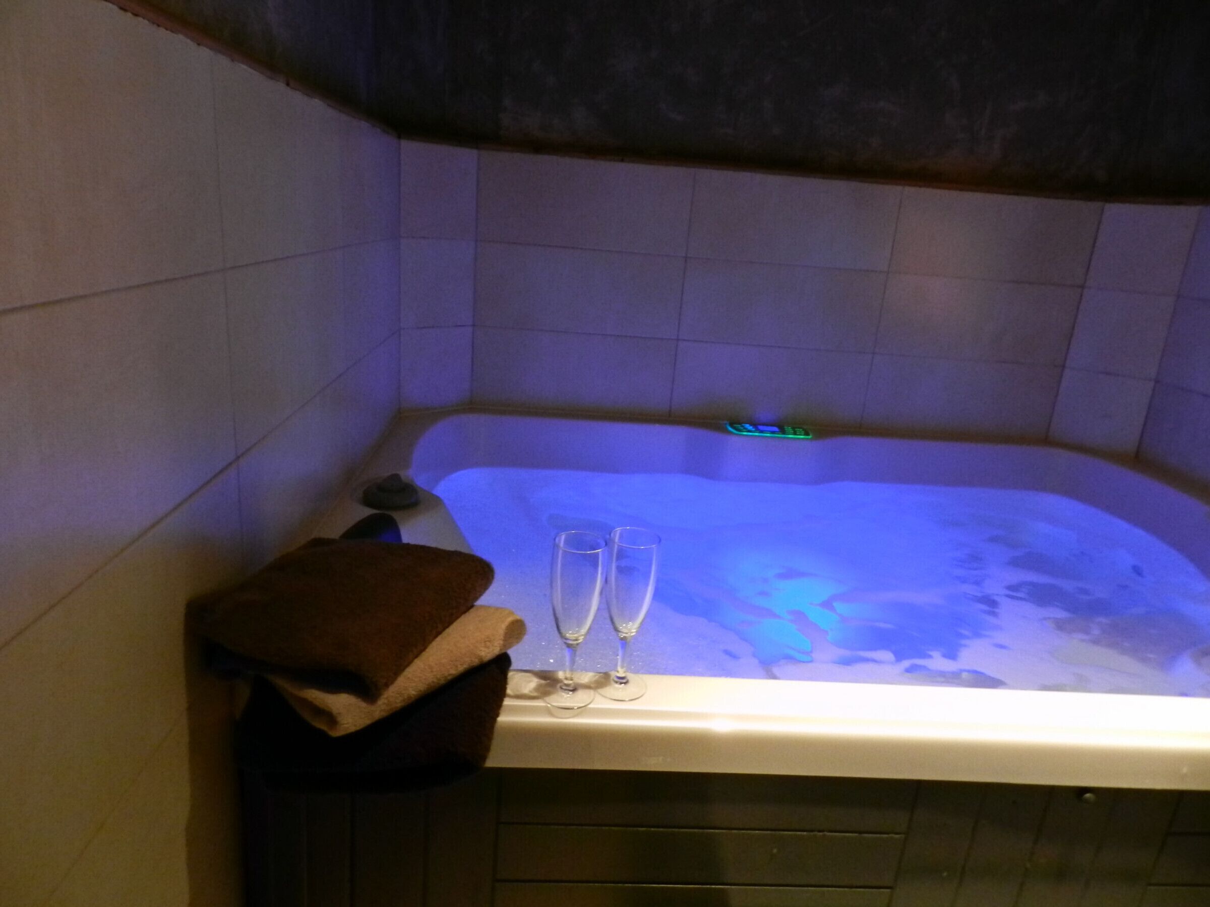 A bathtub with a blue light, two glasses, and a brown towel.