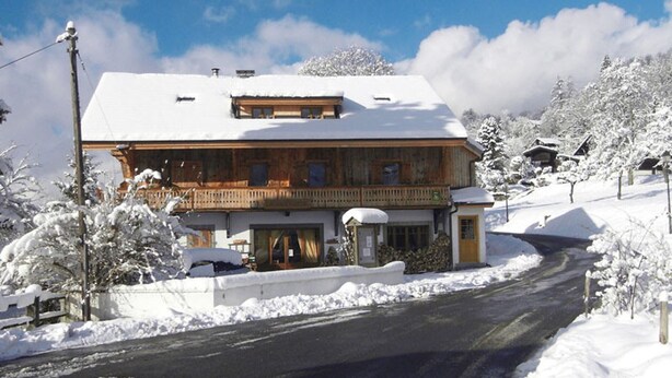 Un edificio de madera de dos pisos con un balcón, rodeado de árboles nevados y un cielo despejado.