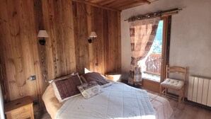 Un dormitorio con paneles de madera, una cama, dos lámparas fijadas a la pared, una ventana con cortinas y una silla.
