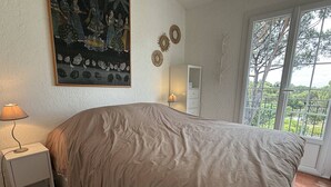 Un dormitori amb un llit, una tauleta de nit, una làmpada, un quadre i una finestra amb vistes.