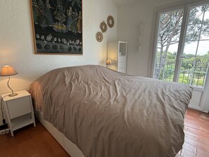 Ein Schlafzimmer mit Bett, Nachttisch, Lampe, Gemälde und einem Fenster mit Blick.