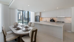 A modern kitchen with white cabinets, a marble countertop, and a dining area with a table set for four. - Modern Beachfront 3BR Apt | Near Marina & JBR (Dubai)